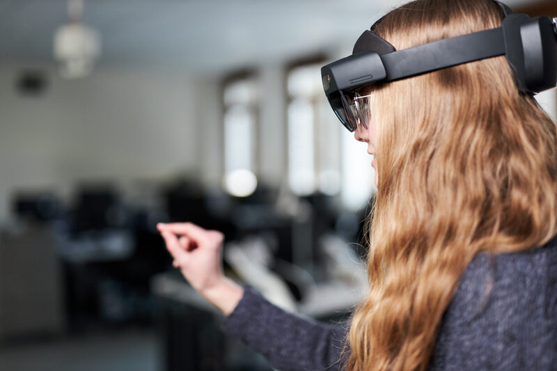 Photo of a person wearing VR glasses. She reaches in front of her with her right hand.