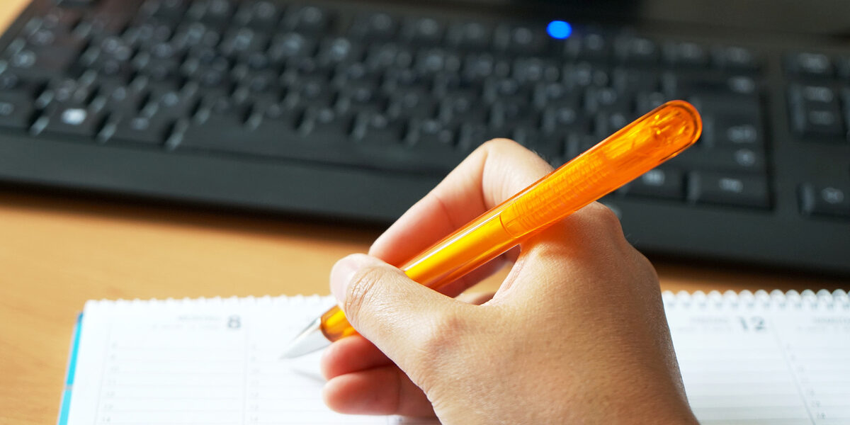 A hand writing something down in a calendar with a pen.