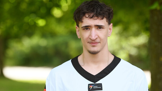 A man in a white top with a black collar and the German flag on his sleeve looks into the camera.