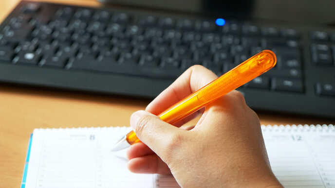 A hand writing something down in a calendar with a pen.