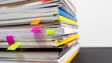 Close-up of a pile of files and documents with colorful post-its sticking out in some places.