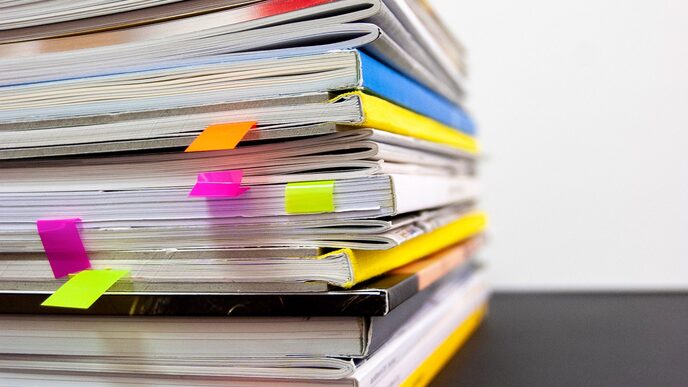 Close-up of a pile of files and documents with colorful post-its sticking out in some places.