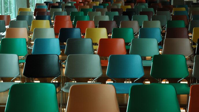 Frontal view of a room with several rows of empty chairs with colorful chair backs.