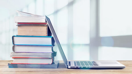 Photo of an opened laptop with its screen touching a stack of books behind it.