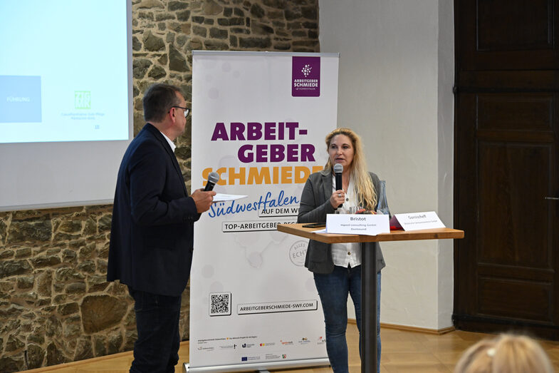 An einem Tisch stehend präsentieren Ansgar Rahmacher, Marcel Mitas und Leon Sachweh Assistenzsystem für die Gesundheits- und Pflegebranche.