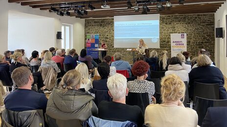 An einem Tisch stehend präsentieren Ansgar Rahmacher, Marcel Mitas und Leon Sachweh Assistenzsystem für die Gesundheits- und Pflegebranche.