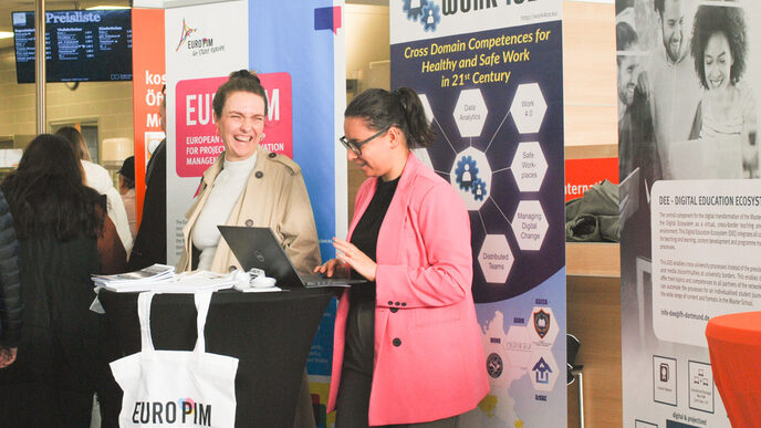 Two young women are laughing and talking at a laptop at a booth, at the "Marketplace of Opportunities"__Two young women are laughing and talking at a laptop at a booth, at the "Marketplace of Opportunities"