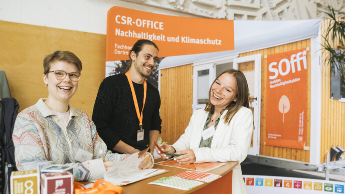 Drei Rezeptionistinnen stehen hinter dem Tresen und lachen freundlich in die Kamera