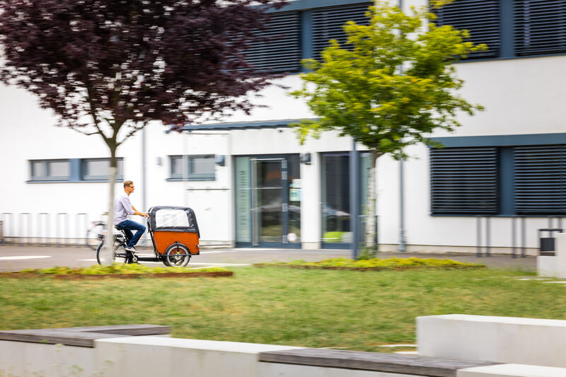 Foto Foto von einem Mann auf einem Lastenfahrrad auf dem FH-Gelände fährt.