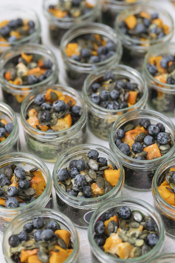 Auf dem Bild ist ein Ausschnitt von einem Buffet zu sehen auf dem nur Gläser aneinandergereiht stehen. In den Gläsern ist ein bunter Salat.