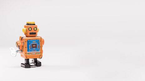 Foto von einem orangenen Blechroboter vor weißem Hintergrund