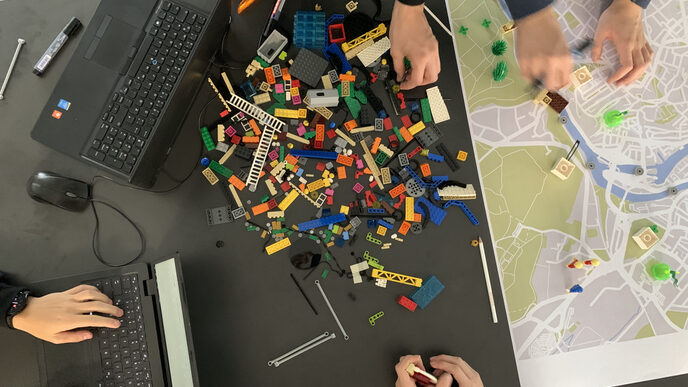 View from above of a table with laptops, a map and Lego bricks in the middle and hands of workshop participants.