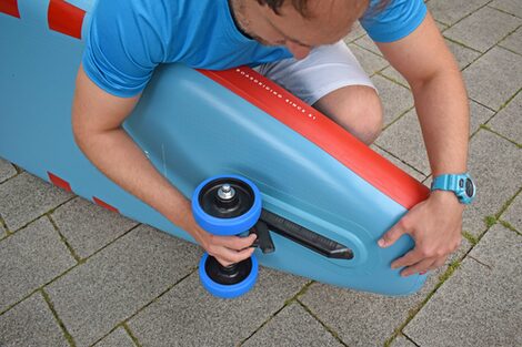 One person attaches two rollers under a stand-up paddle board.