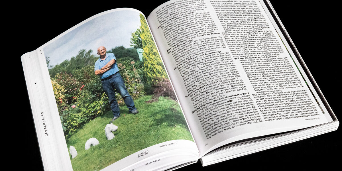 Ein aufgeschlagenes Buch, auf der einen Seite ein große Foto von einer männlich gelesenen Person in einem Garten, auf der anderen Seite Text.