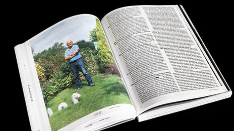 Ein aufgeschlagenes Buch, auf der einen Seite ein große Foto von einer männlich gelesenen Person in einem Garten, auf der anderen Seite Text.