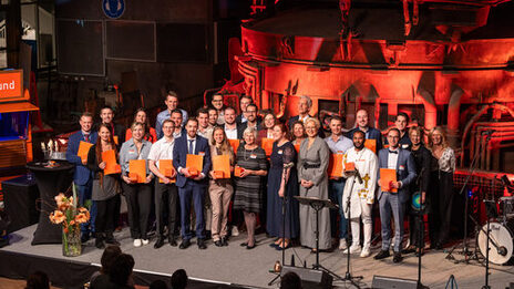 Many people stand on the stage with certificates in their hands.