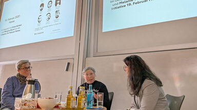 Menschen vor einer Leinwand in einem Hörsaal sprechen miteinander.