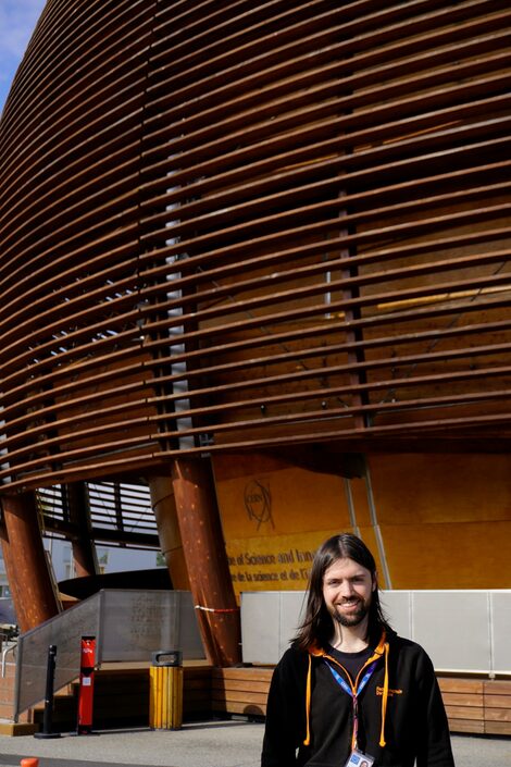 A person is standing in front of a building. The façade is curved and consists mainly of cross beams.