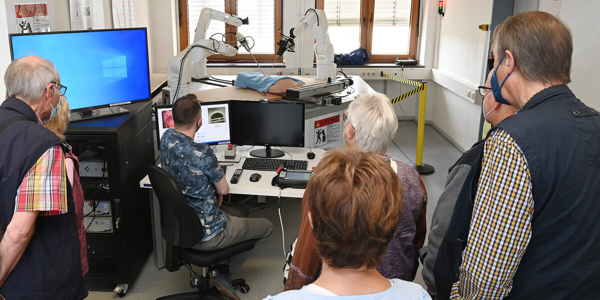 Eine Gruppe Menschen beobachtet die Bewegungen medizinischer Roboterarme.