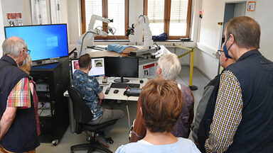 Eine Gruppe Menschen beobachten die Bewegungen medizinischer Roboterarme.