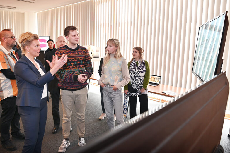 Several people stand in front of large screens in a somewhat darkened room.