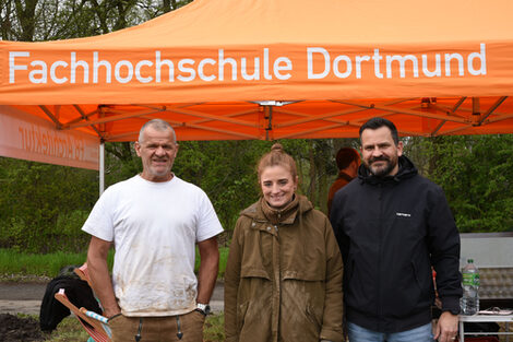 Group photo with three people standing next to each other in front of a tent roof with Fachhochschule Dortmund written on it