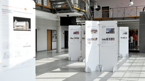 Ausstellung im Foyer des Fachbereichs mit freistehenden weißen Tafeln, auf denen Architekturprojekte zum Deutschen Ziegelpreis 2024 präsentiert werden.