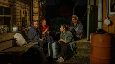 Four people are sitting in the dark between two houses.
