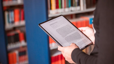 Foto von einem Tabelt in der Hand von jemanden, der in einer Bibliothek steht.