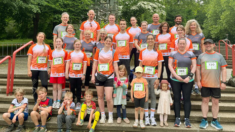 A group of people stand in several rows on a staircase, all wearing Fachhochschule Dortmund running shirts and facing the camera.