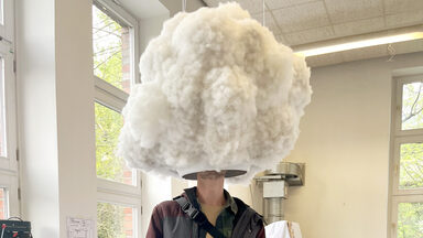 A person stands under a cloud-like structure with an opening at the bottom that covers the person's head.