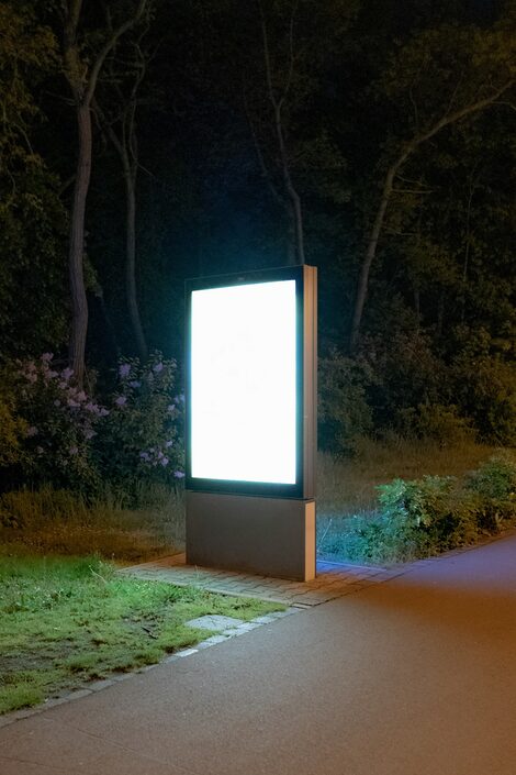 Vor einem dunklen Waldstück leuchtet ein Werbe-Display.