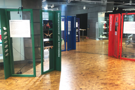 Farbig- und teiltransparente Ausstellungselemente zu den Themen Geschlecht, Menschen mit Behinderung und Generationen stehen in einer Halle.