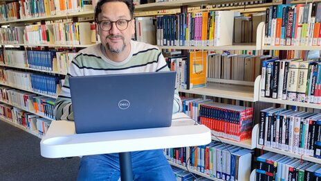 Foto von einem Mann auf einem Indoor-Fahrrad mit kleinem Tisch, auf dem ein Laptop steht__Photo of a man sitting on an indoor bicycle with a small table, a notebook is placed on the table