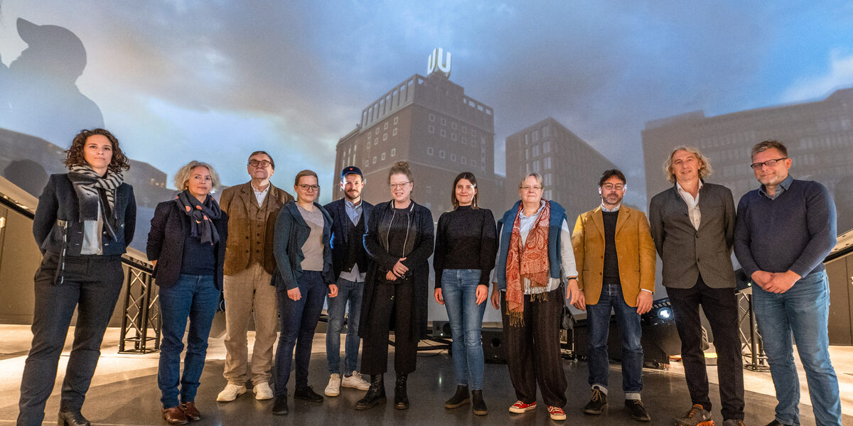 Gruppenbild mit 11 Personen, die nebeneinander vor einer Projektion stehen, die das Dortmunder U von außen zeigt.