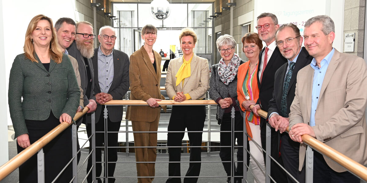 Eleven people stand around the banister of a staircase and look into the camera.