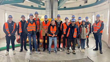 A group of people wearing high-visibility vests and helmets stand in a round building.