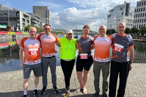 Sechs Personen stehen nebeneinander vor einem See.