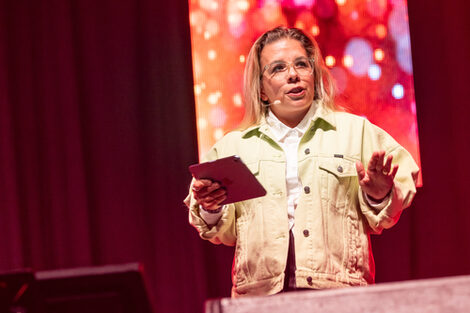 A person with a microphone on their mouth and text cards in their hand speaks to an audience.