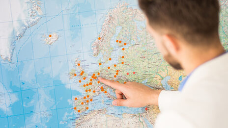 Photo of a person pointing at a large world map with places marked with orange dots