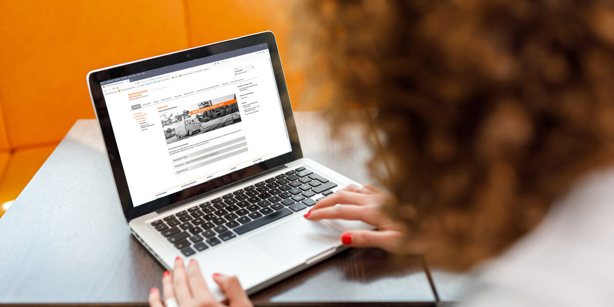 Foto einer jungen am Laptop, im Hintergrund sind orangefarbene Sitzmöbel. __ Young woman at the laptop, in the background there are orange colored chairs.