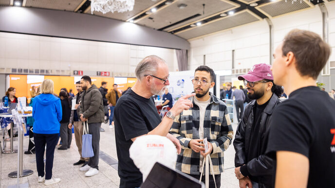 Several people talking to each other. Other exhibition stands can be seen in the background.