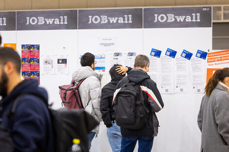 Studierenden betrachten die Aushänge an einer Wand mit dem Schriftzug "JOBwall"
