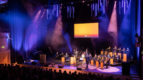 Auf der Bühne im Konzerthaus spielt eine Big-Band. Die Notenständer sind mit "50 Jahre Fachhochschule Dortmund" verhüllt. Die Bühne erstrahlt in orangefarbenem Licht.