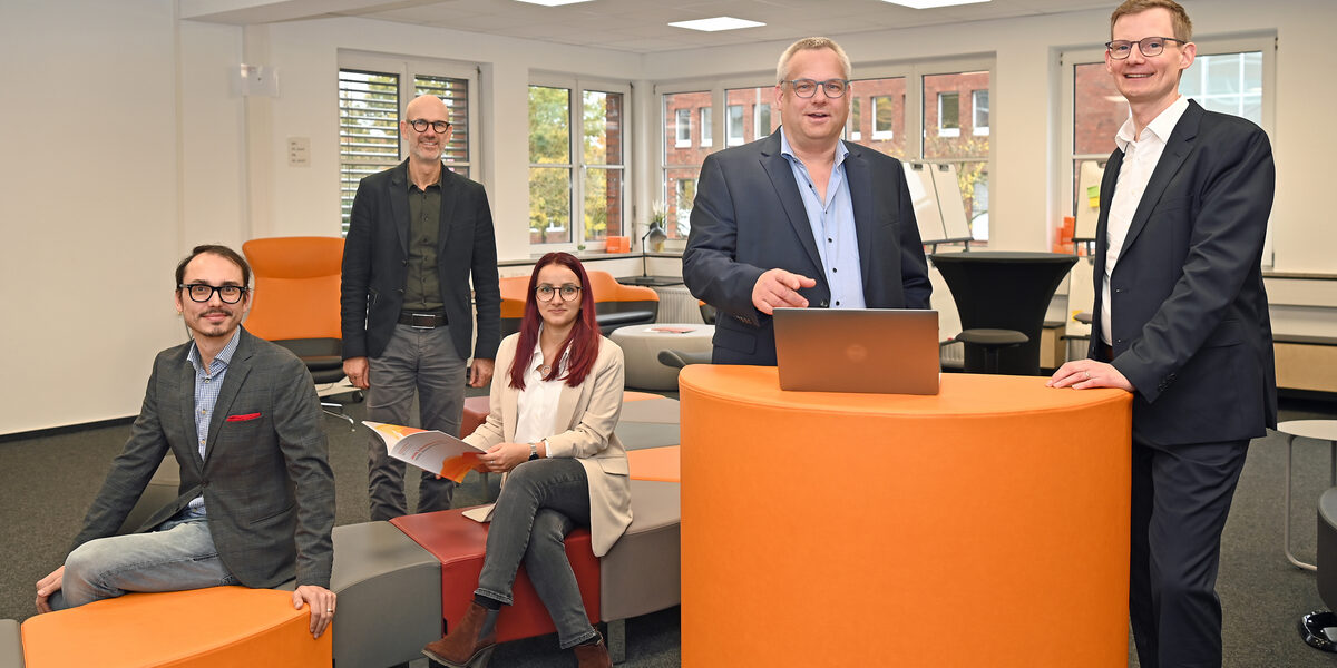 A group of people stand and sit at and around an orange desk in the User Innovation Center.