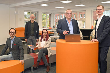 Eine Personengruppe steht und sitzt an und um einem orangefarbenen Pult im User Innovation Center.