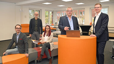 Eine Personengruppe steht und sitzt an und um einem orangefarbenen Pult im User Innovation Center.