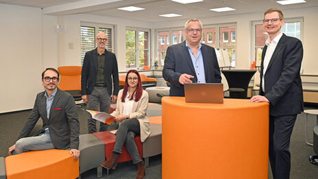 Eine Personengruppe steht und sitzt an und um einem orangefarbenen Pult im User Innovation Center.