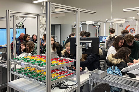 A group of people of school age look at and examine the devices in a laboratory.