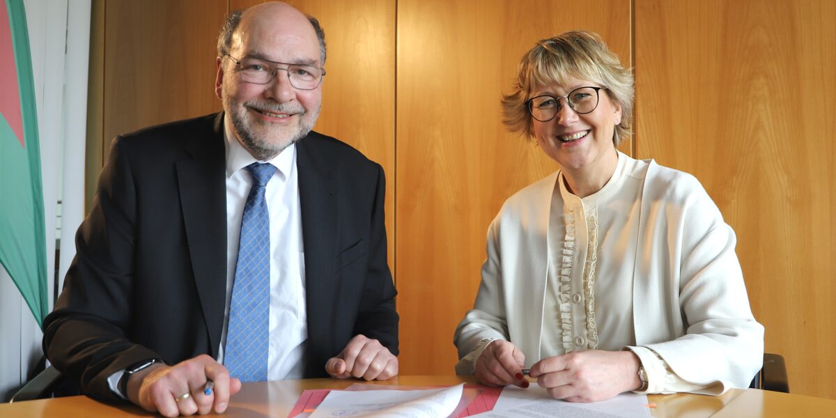 Two people are sitting next to each other at a table on which papers are lying.